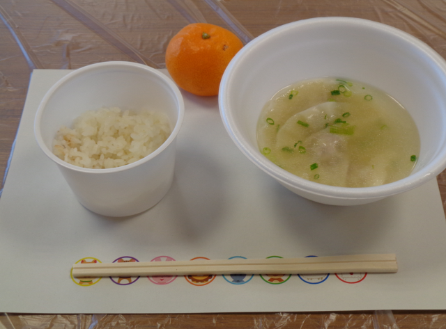 ランチョンマットの上に乗せた、水餃子とごはん、デザートのみかん